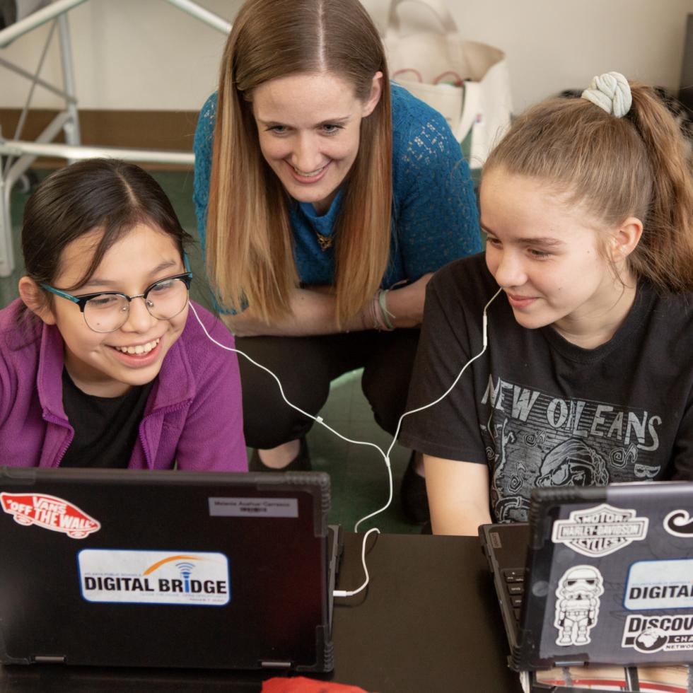 Female English teacher with two female students sharing earbuds