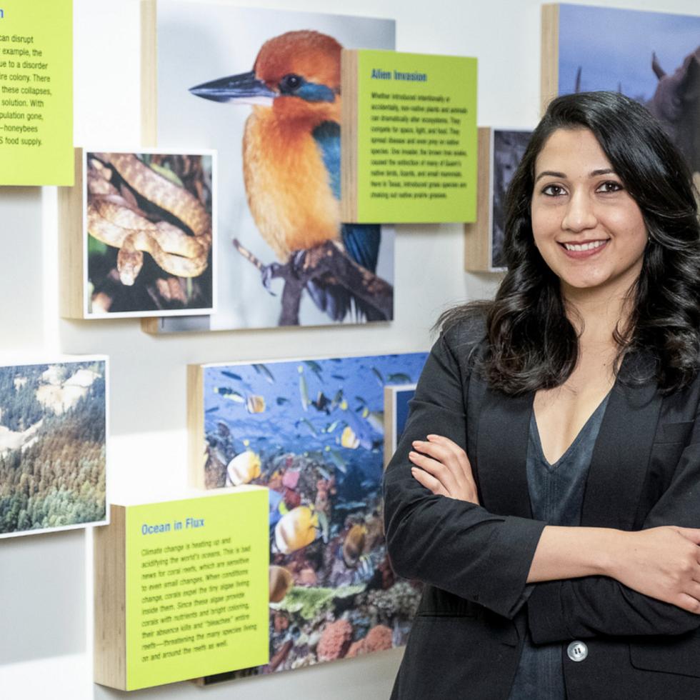 Photo of Shyla Raghav posing in front of a wall with information about different types of birds
