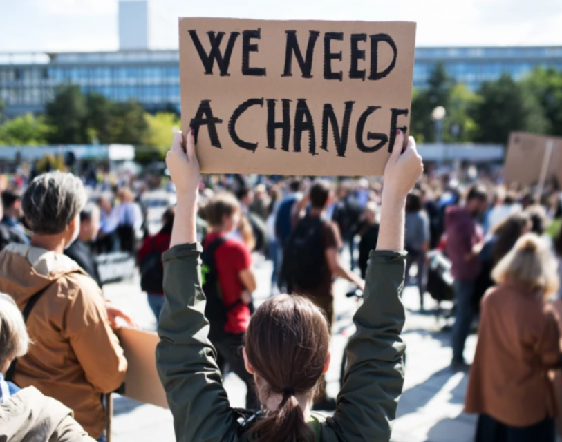 Girl holding a sign that says "We need a change"