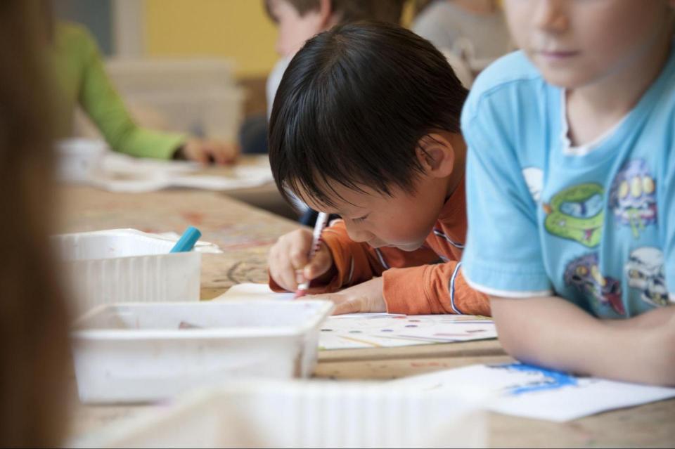 Image of child using a writing tool on a paper, at a table. 