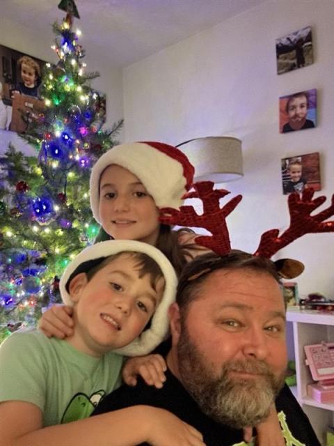 Jeff Davis with his two children: Zoe (9) and Austin (7) wearing red Christmas hats next to a decorated Christmas Tree