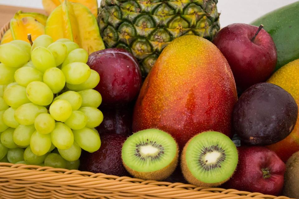 A close-up of fruit in a basket - grapes, starfruit, pineapple, apples, plums, mangoes, kiwis