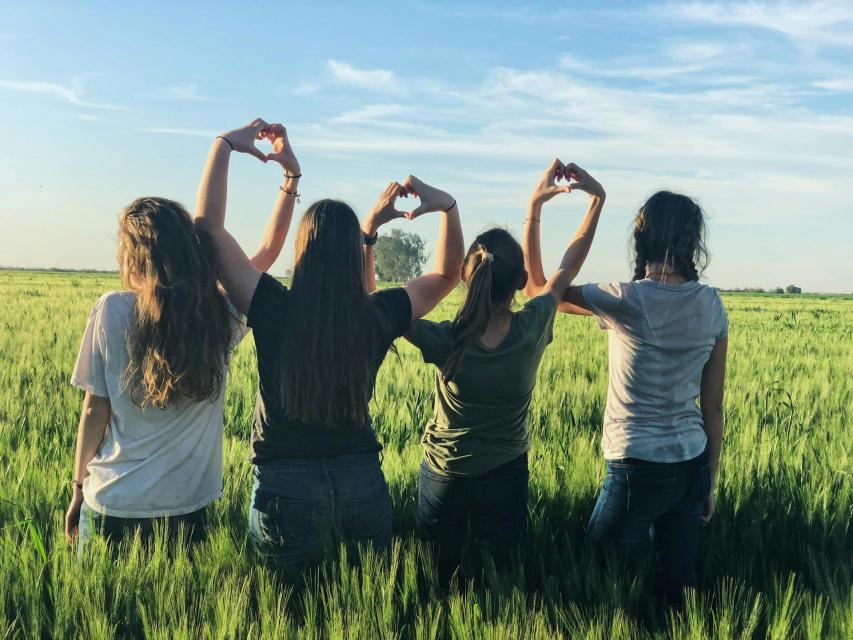 Four girls with their backs turned to the camera making hearts with their hands