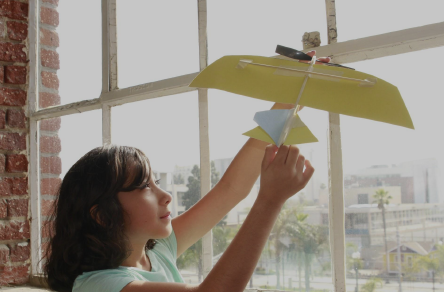 Girl holding paper airplane to a window.