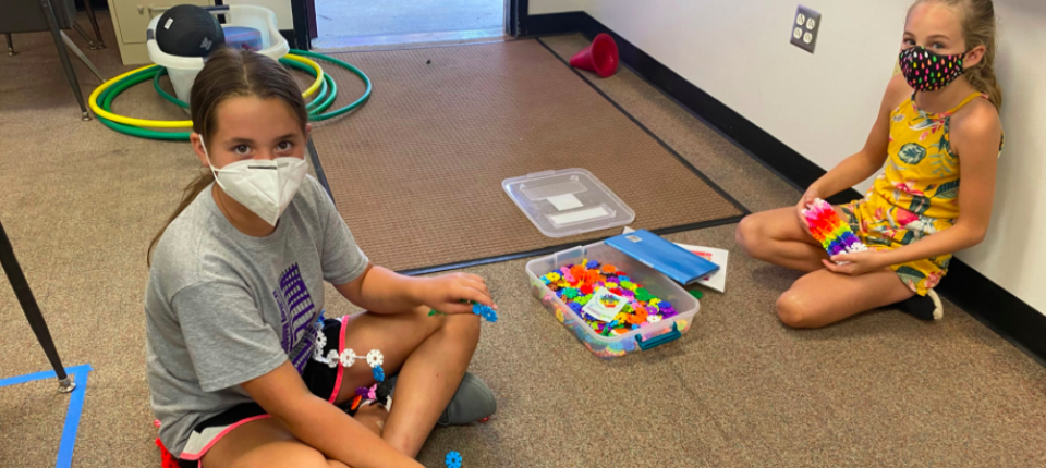 Two students working on the floor wearing masks.