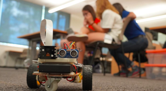 Close-up of a robot on the ground with students in the background.