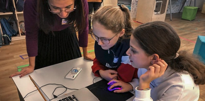 Three girls huddled around a laptop working on a project