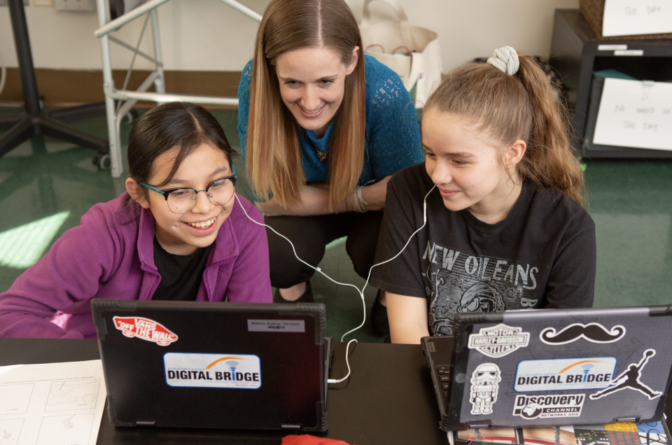 Female English teacher with two female students sharing earbuds