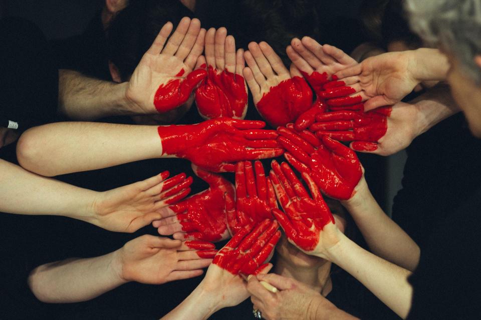 A red heart painted on human hands.