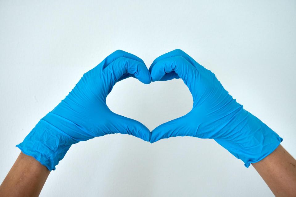 Human hands wearing blue gloves and forming a heart. 