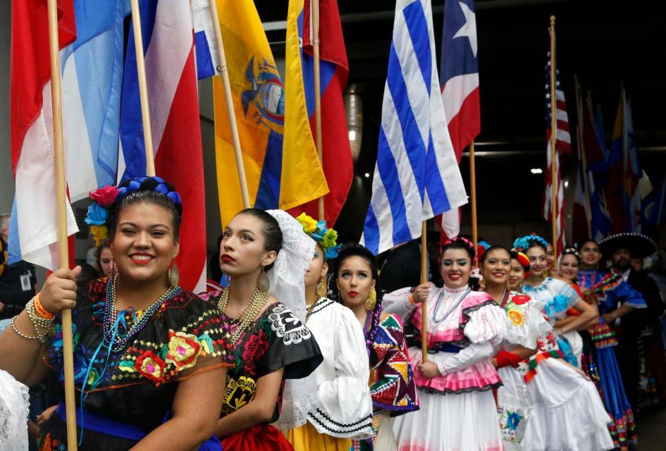 Group of women in native Mexican dresses lining up holding flags before doing a dance.