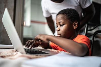 Child typing on laptop with parent in the background