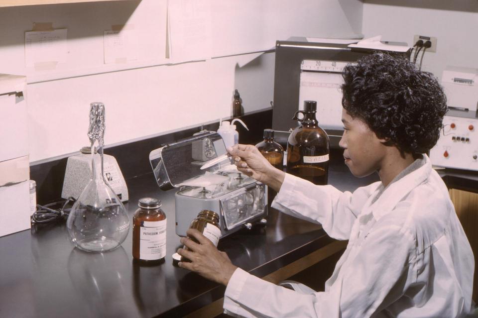 This historic 1965 photograph, depicted a laboratory technician, as she was measuring out various powdered chemicals, which would subsequently be combined in order to formulate reagents to be used in conjunction with an AutoAnalyzer.