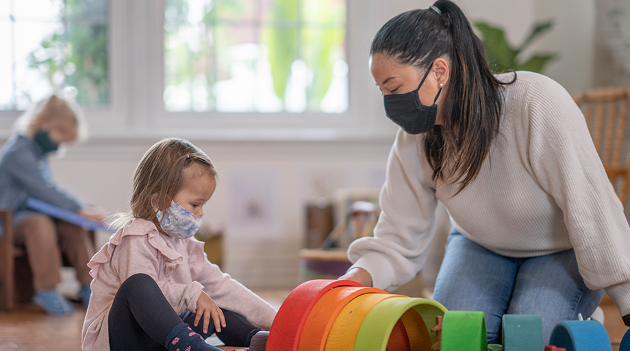 Child and adult, wearing mask, in a learning environment. 