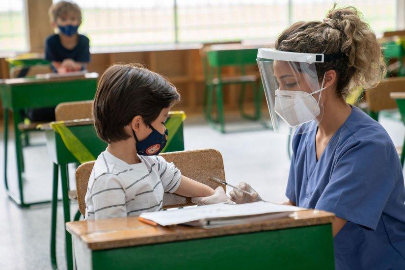 Nurse giving student COVID-19 vaccine in classroom