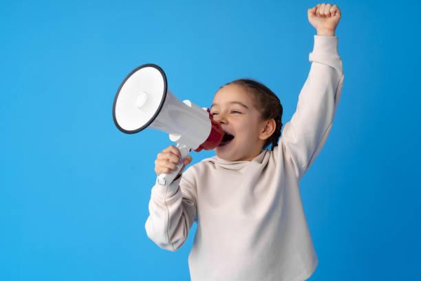 young child holding a megaphone raising her left arm like a cheer  