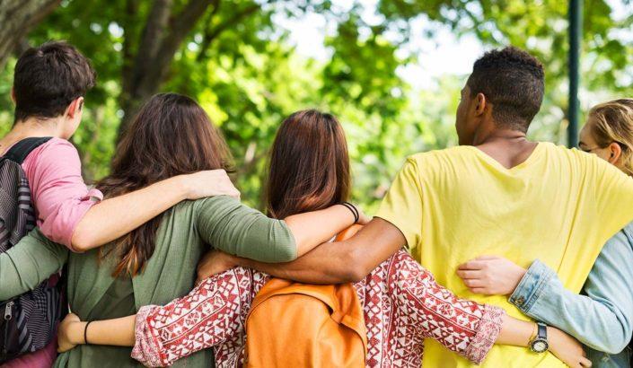 Group of children with their backs facing the camera with their arms around each other's shoulders.