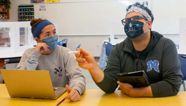 Two educators wearing masks sitting at a desk.