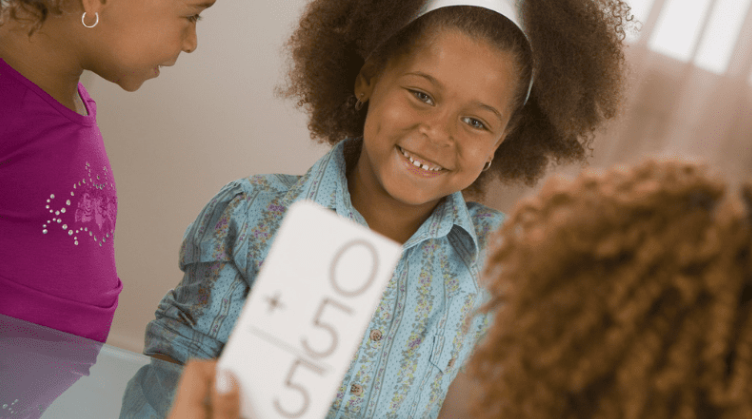 Girl smiling into the camera using flashcards with a teacher