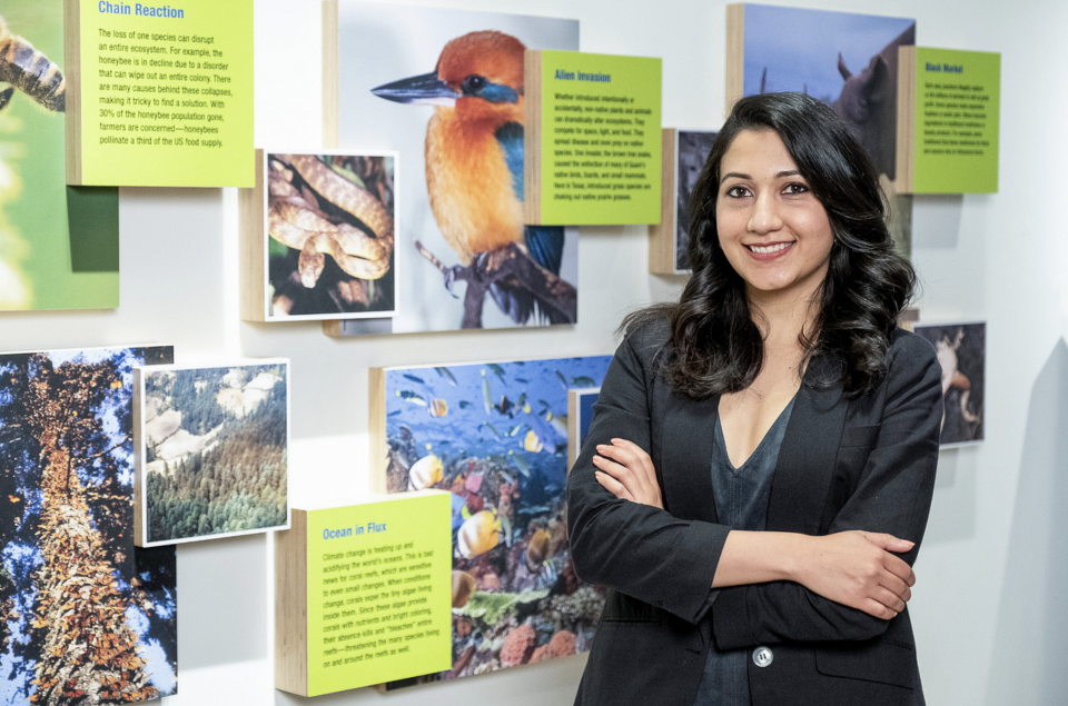 Photo of Shyla Raghav posing in front of a wall with information about different types of birds